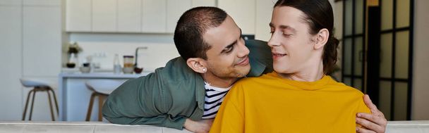 Una joven pareja gay se sienta en un sofá en su apartamento moderno, disfrutando de la compañía de los demás. - Foto, imagen