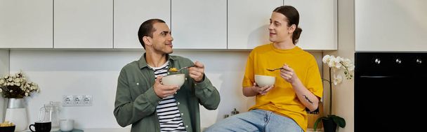 Молодая гей-пара наслаждается случайным завтраком вместе в своей современной квартире. - Фото, изображение