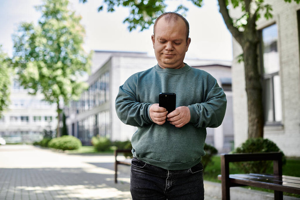 Un hombre con inclusividad camina por la ciudad, usando su teléfono. - Foto, imagen