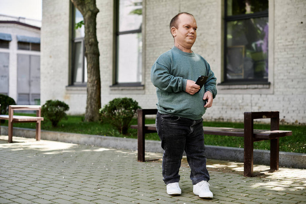 Un hombre con inclusividad con un teléfono en mano camina por un banco en un entorno urbano. - Foto, imagen