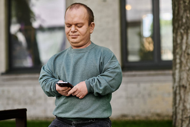 Чоловік з інклюзивністю в зеленому светрі перевіряє свій телефон під час прогулянки в міській обстановці. - Фото, зображення