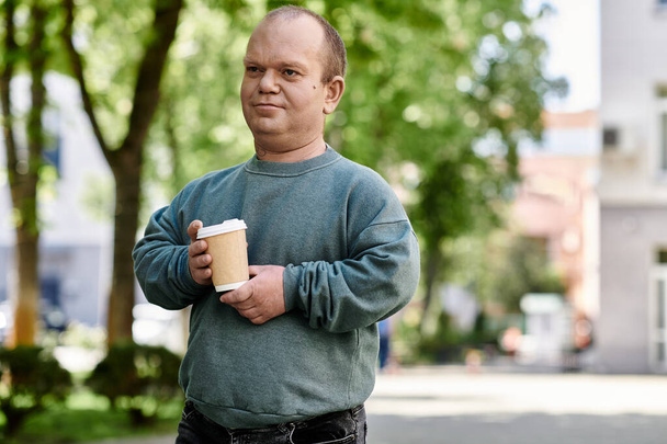 Egy inkluzivitású férfi kávét iszik egy napsütéses napon egy városi parkban.. - Fotó, kép