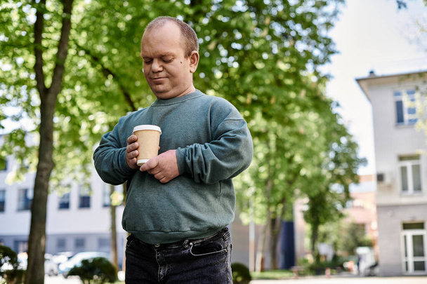 Человек с инклюзивностью наслаждается кофе в теплый день, окруженный деревьями. - Фото, изображение