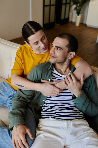 Een jong homo paar knuffelt op een bank in hun moderne appartement, genieten van kwaliteit tijd samen. - Foto, afbeelding