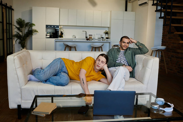 Ένα νεαρό γκέι ζευγάρι περνάει ένα βράδυ χαλαρώνοντας σε ένα λευκό καναπέ σε ένα μοντέρνο διαμέρισμα. - Φωτογραφία, εικόνα