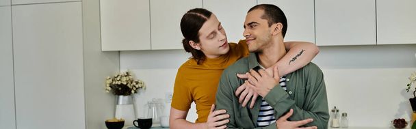 Ένα νεαρό γκέι ζευγάρι μοιράζεται μια τρυφερή στιγμή στοργής στη μοντέρνα κουζίνα του διαμερίσματός του.. - Φωτογραφία, εικόνα