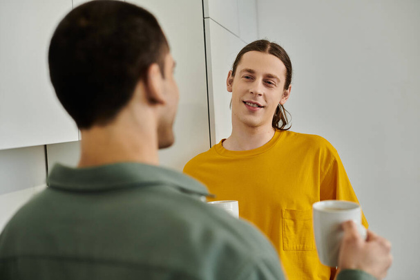 Ένα νεαρό γκέι ζευγάρι απολαμβάνει μια περιστασιακή συζήτηση στο μοντέρνο διαμέρισμά του.. - Φωτογραφία, εικόνα