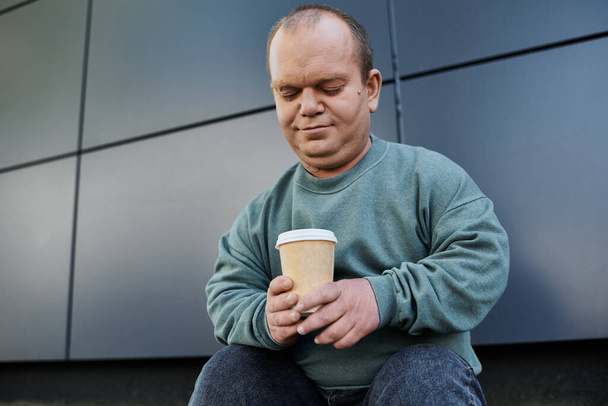 Człowiek z inkluzją siedzi na zewnątrz, myśląc o filiżance kawy.. - Zdjęcie, obraz