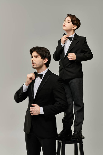 Un padre e suo figlio stanno fianco a fianco, entrambi vestiti con abiti neri e papillon.. - Foto, immagini