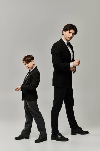 Πατέρας και γιος ποζάρουν με ασορτί κοστούμια σε γκρι φόντο.. - Φωτογραφία, εικόνα