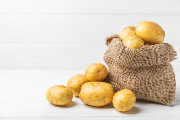 Young potatoes. Fresh potatoes on a wooden background. potato in burlap sack. Harvesting collection. organic, freshly dug potatoes. Agricultural background. Vegan. Vegetables.Place for text.Copy space - Photo, Image