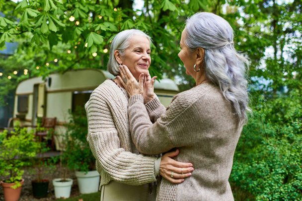 Dvě ženy středního věku v svetrech se vřele objímají venku. - Fotografie, Obrázek