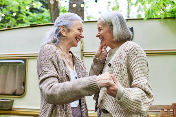 Dvě ženy středního věku se společně smějí před svou dodávkou v zeleném lese. - Fotografie, Obrázek