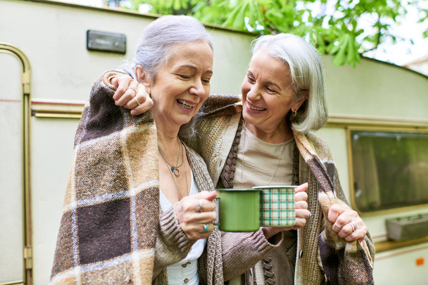 Duas mulheres lésbicas de meia-idade desfrutam de uma xícara de café enquanto acampam na floresta. - Foto, Imagem