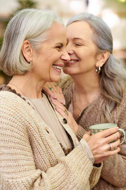 Two women, an older lesbian couple, are close together in a forest setting. They appear to be camping, and one of them is holding a mug. - Photo, Image