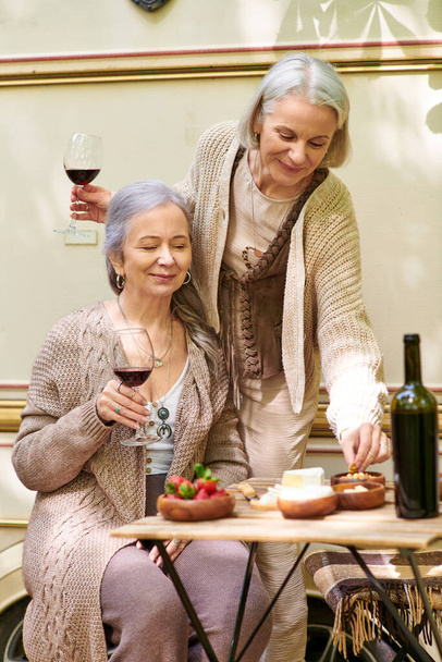 Дві лесбіянки середнього віку насолоджуються вином і закусками під час кемпінгу біля свого фургона в пишному зеленому лісі. - Фото, зображення