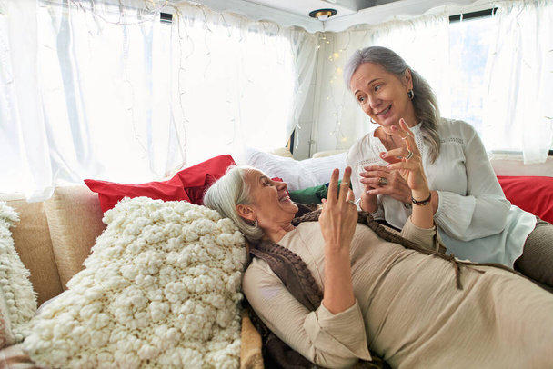 Una coppia lesbica, entrambi di mezza età con i capelli grigi, condividono un momento spensierato mentre si rilassa in un camper. - Foto, immagini