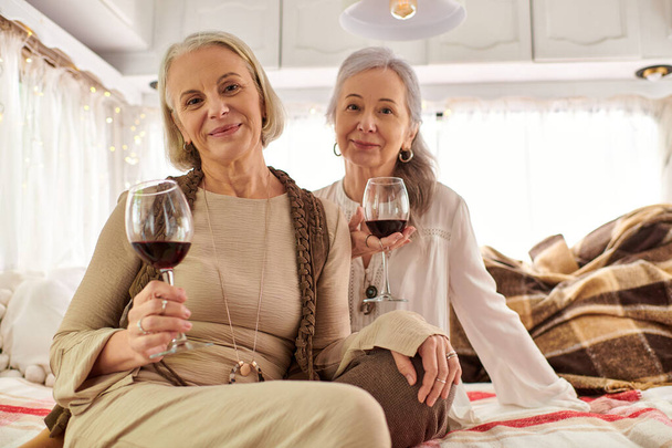 Una pareja lesbiana disfruta de una copa de vino dentro de su casa rodante durante un viaje por carretera. - Foto, imagen