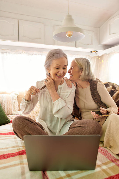 Zwei Frauen mittleren Alters lachen und teilen einen Moment in ihrem Wohnwagen. - Foto, Bild