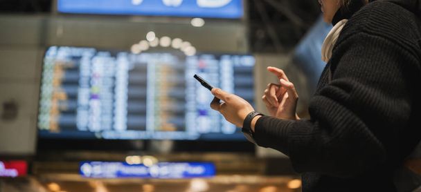 Lähikuva naisesta tarkistamassa puhelinta lentoaseman terminaalissa, Käsite matka ja teknologia. - Valokuva, kuva