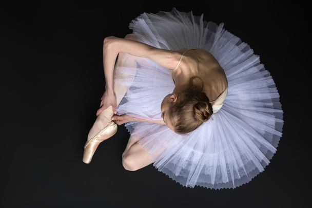 Young ballet dancer tying pointe sitting on the floor - 写真・画像