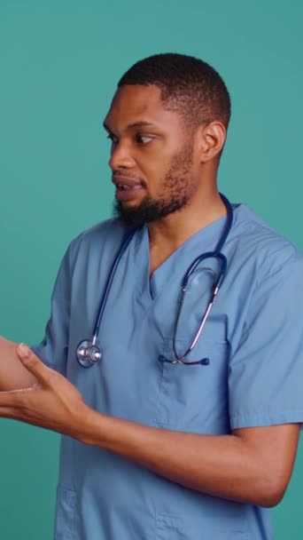 Вертикальное видео Портрет африканской американской медсестры, указывающей руками на пустое пространство, делающей рекламу, разговаривающей с аудиторией. Сотрудник здравоохранения делает рекламную рекламу, показывает текст копии, студию - Кадры, видео