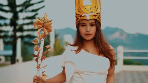 A woman in traditional attire and a golden headdress stands outdoors with mountains in the background. - Footage, Video