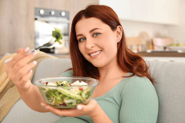 Mladá těhotná žena jí čerstvý zeleninový salát sedí na pohovce doma - Fotografie, Obrázek