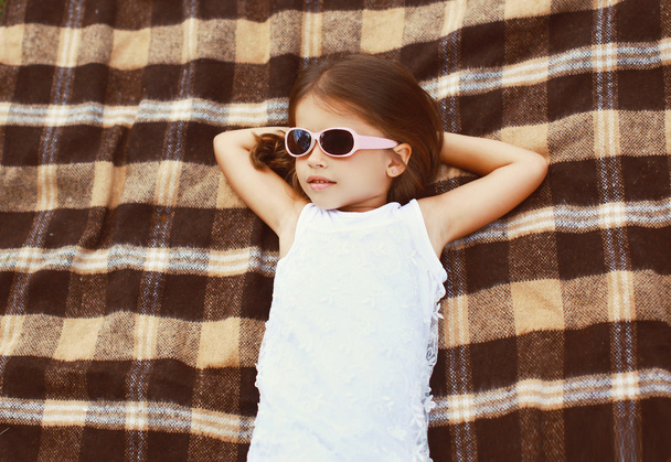 Little girl in sunglasses lying on the plaid, top view - Fotografie, Obrázek