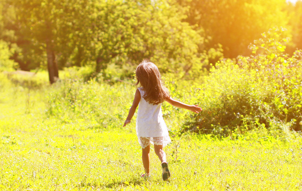 Silhouette eines kleinen Mädchens, das an einem sonnigen Sommertag auf dem Feld läuft - Foto, Bild