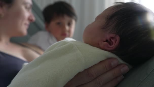 Mother and older sibling looking at newborn baby, capturing a moment of familial love and connection in the hospital bed. tender interaction and bond between the mother, older child, and newborn - Imágenes, Vídeo