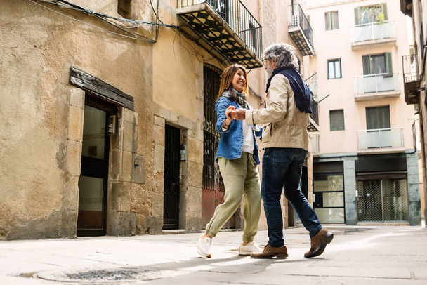 Счастливая пожилая пара туристов, весело танцующих на городской улице во время отпуска. Счастье и праздничный образ жизни. - Фото, изображение