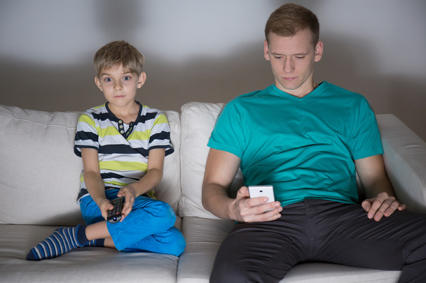 Child watching tv and dad using phone - Foto, Imagen