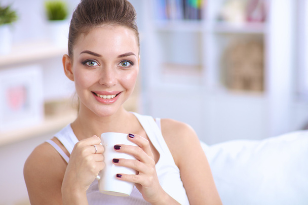 Portrait of oung beautiful woman with a cup on sofa at home - Photo, Image