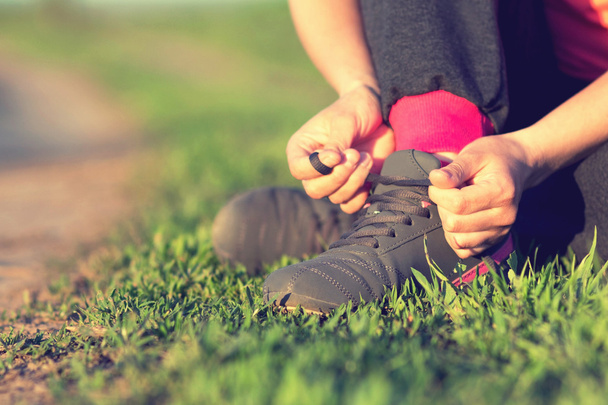 Girl tying shoelaces shoes sitting on the grass - 写真・画像