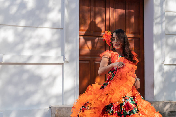 Donna sorridente in vibrante abito tradizionale ballare all'aperto contro una porta di legno in una giornata di sole. - Foto, immagini
