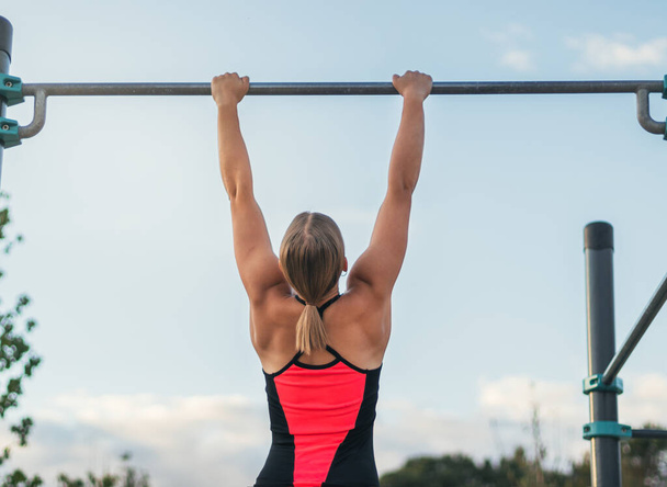 visão traseira de uma mulher atleta fazendo pull ups em um bar ao ar livre. calistênicos - Foto, Imagem