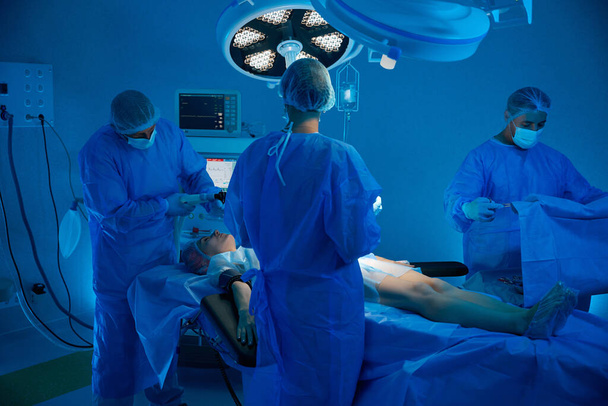 Doctor anesthetist applying anesthesia machine to female patient with team of skilled surgeons in operating room - Photo, Image