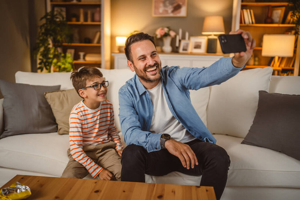 Vader en zoon gebruiken mobiele telefoon voor videogesprekken thuis - Foto, afbeelding