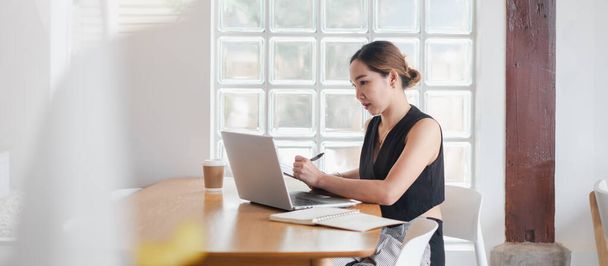 Jovem mulher trabalhando em um laptop em um café moderno, com café e notebook, luz natural através da janela do bloco de vidro. - Foto, Imagem