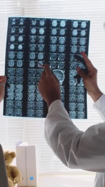 Zoom avant vertical gros plan d'un neurologue indien démontrant une IRM au patient, indiquant des anomalies après une lésion cérébrale, lors d'une consultation à l'hôpital - Séquence, vidéo