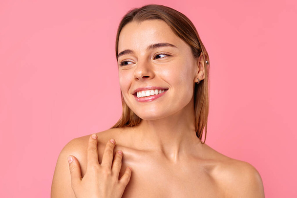 Eine fröhliche junge Frau strahlt vor rosa Hintergrund ein strahlendes Lächeln aus, das ihre klare, strahlende Haut und natürliche Schönheit zur Geltung bringt. Perfekt für Wellness-, Pflege- und Positivitätskonzepte. - Foto, Bild