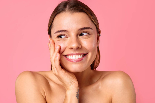 Radosna młoda kobieta błyska jasnym uśmiechem na różowym tle, pokazując jej czystą, promienną skórę i naturalne piękno. Idealny do wellness, pielęgnacji skóry i koncepcji pozytywności. - Zdjęcie, obraz
