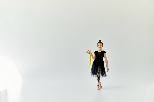 Młoda dziewczyna z protezą nogi ćwiczy gimnastykę z żółtą obręczą w białym studiu. - Zdjęcie, obraz