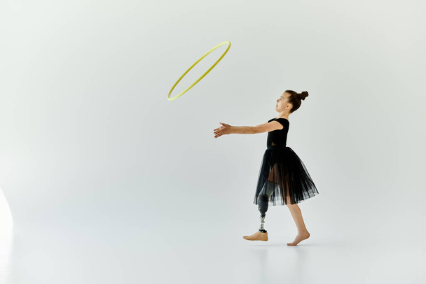 Ein junges Mädchen mit Beinprothese turnt mit einem Hula-Hoop-Reifen in einem weißen Studio. - Foto, Bild