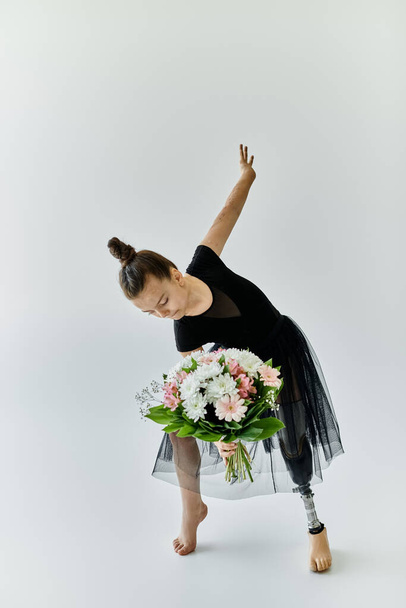 A young girl with a prosthetic leg performs a gymnastic pose while holding a bouquet of flowers. - Foto, Imagen