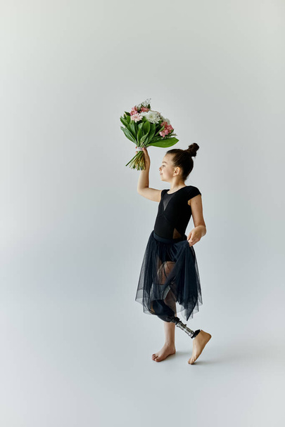 Uma jovem com uma perna protética pratica ginástica enquanto segura um buquê de flores. - Foto, Imagem