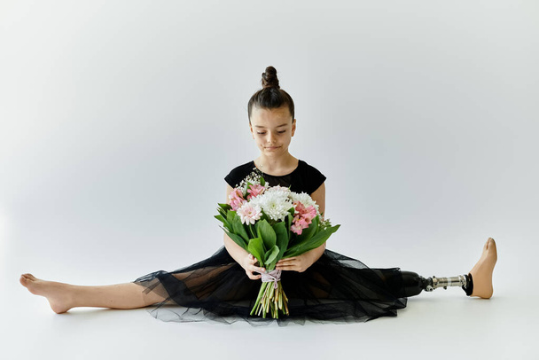 Młoda dziewczyna z protezą nogi siedzi w rozdwojonej pozycji, trzymając bukiet kwiatów. - Zdjęcie, obraz