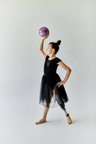 Een jong meisje in een zwarte maillot en rok oefent gymnastiek met een prothese been. - Foto, afbeelding