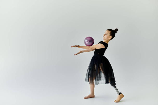 Ein junges Mädchen mit Beinprothese führt rhythmische Gymnastik mit Ball aus. - Foto, Bild
